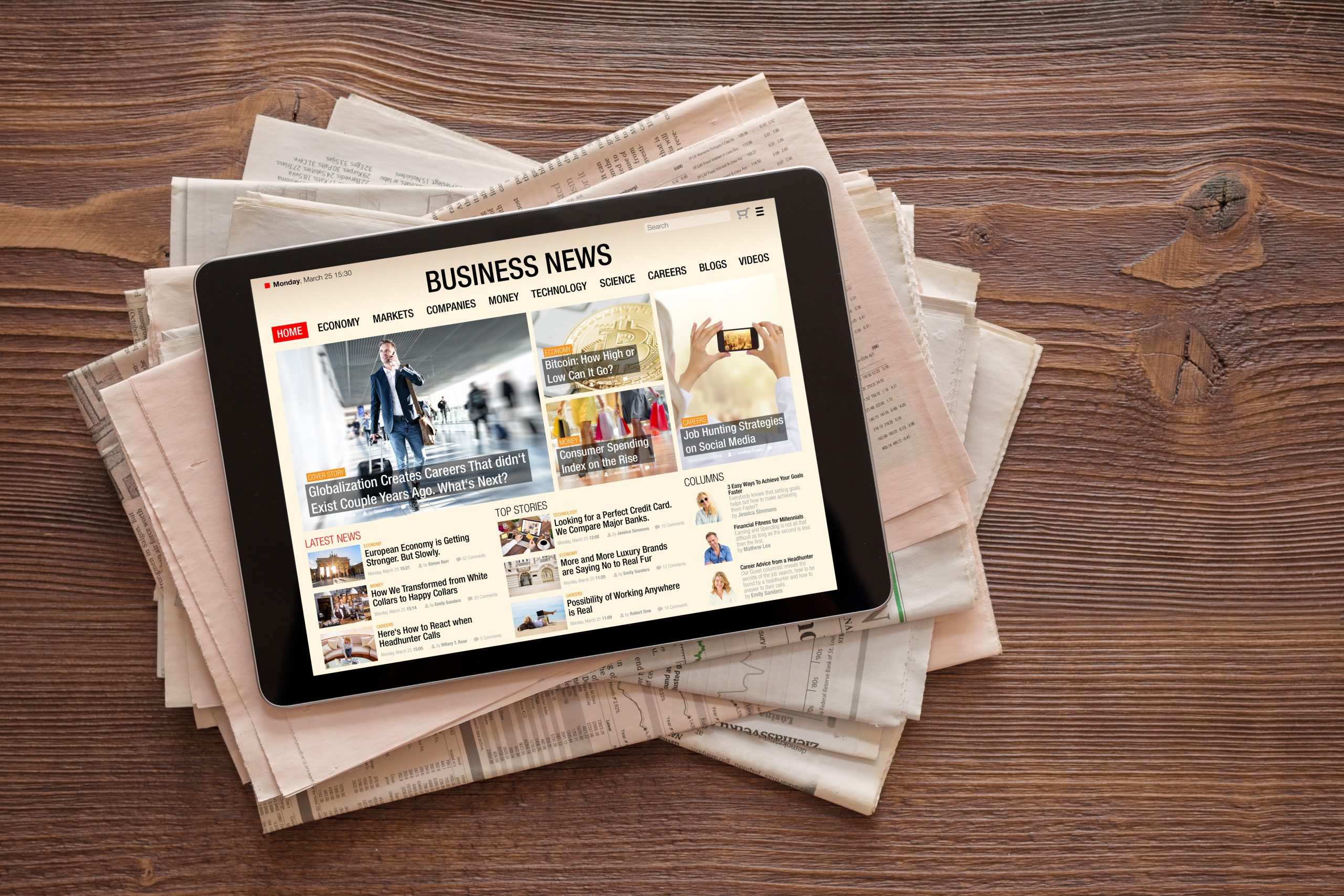 Tablet with business news website on stack of newspapers.